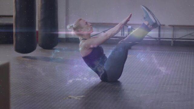 Performing mid-adult woman in dark tanktop lifting into V-sit at gym studio, with nebula overlay