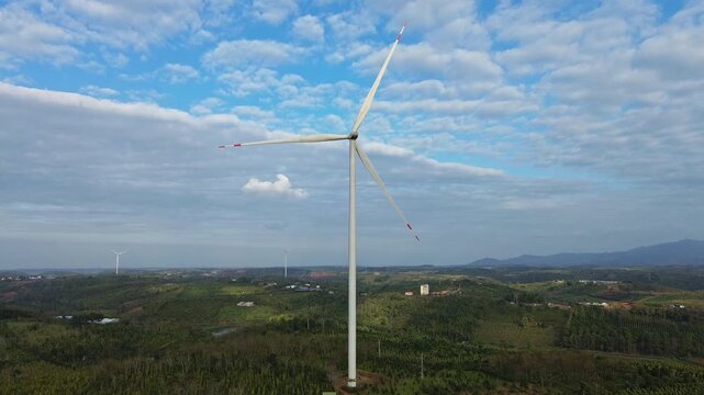 Aerial still shot showing a windmill in its entirety on green hills in Dak Mil, Central Highlands Vietnam. Scenic view of rural landscape and blue sky.