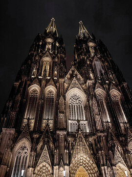 Cologne Cathedral illuminated at night. The Gothic architecture features intricate details and towering spires against a dark sky.