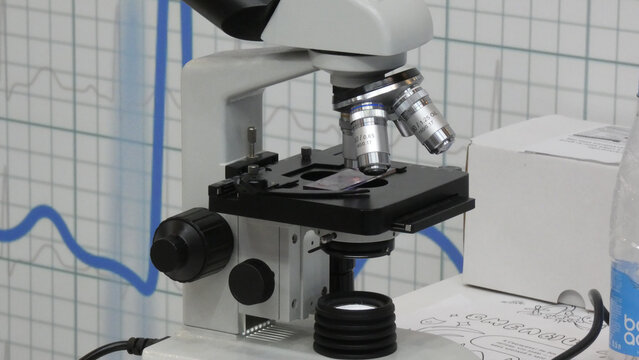 Microscope on lab table shows slides while blue lines mark data on a graph during a research session in a science lab