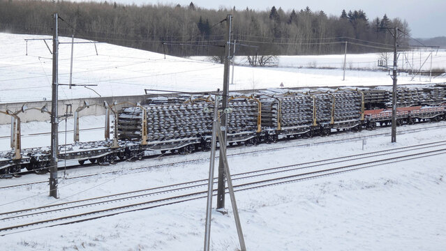Rail transport carrying cargo through snowy landscape in winter season near rural area with trees and fields
