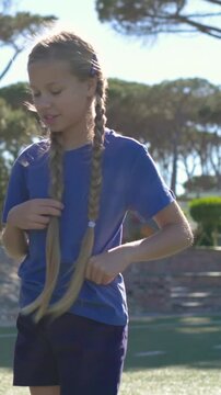 Vertical video: Fixing braids, girl touching hands to greet as friend coming on turf, blue tee