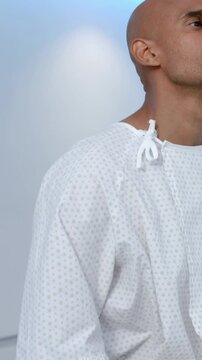 Vertical video: Lifting head man in hospital gown closing eyes as camera moving in clinic for exam