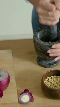 Vertical video: Pressing pestle, cook in plaid prepping, grinding herbs in mortar, chopping onion