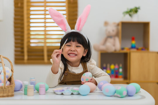 happy preschool child girl wearing bunny ears painting and decorating colorful egg at home on easter day