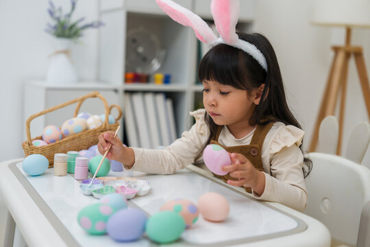 preschool child girl wearing bunny ears painting and decorating colorful egg at home on easter day