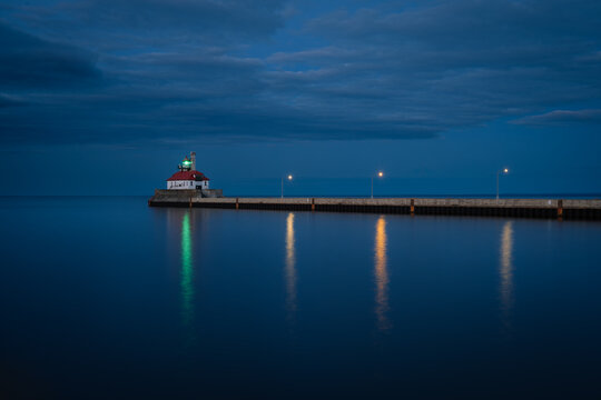 Duluth Harbor South Breakwater Lighthouse illuminated at blue hour on Lake Superior in Duluth, Minnesota, with calm water reflecting pier lights under a dramatic evening sky.