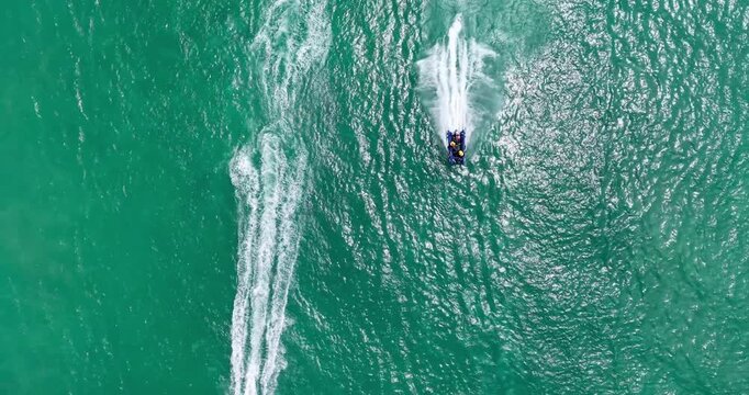 Drone top-down aerial view of a team racing an inflatable rubber duck boat across turquoise ocean water during the Trans Agulhas Challenge. The high-speed boat leaves a long white wake across the sea.
