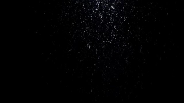 Slow motion static shot of water droplets falling and scattering against black background with top light illumination