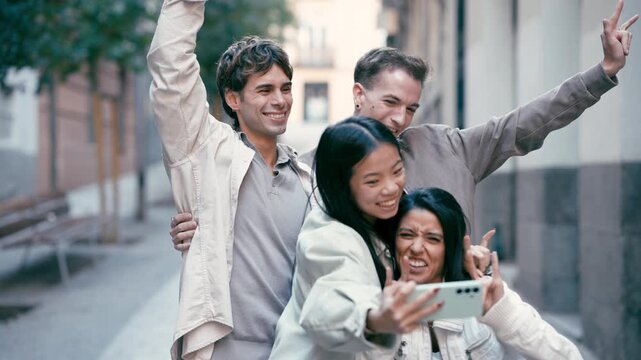 Playful group of four young multicultural friends having fun together and taking a selfie with a smartphone, making funny faces and gestures