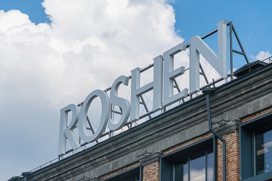 Historic district street scene, confectionery factory Roshen, brickwork buildings, large windowsdoors, contrasting red and black colors, signage ROSHEN, sidewalk - Kyiv, Ukraine 07-13-2025