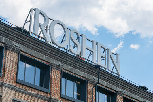 Historic district street scene, confectionery factory Roshen, brickwork buildings, large windowsdoors, contrasting red and black colors, signage AROSHEN, sidewalk - Kyiv, Ukraine 07-13-2025