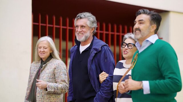 Mature friends enjoying a pleasant walk together through the city. Cheerful senior couples strolling, laughing, and conversing outdoors