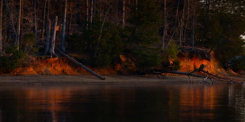 Poster Reflectie Panoramic image of glowing golden light reflected on clay lake shore bluffs and reflected in the quiet water  © Darren Koobs