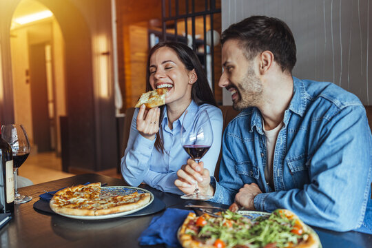 Happy Couple Enjoying Pizza and Red Wine During Casual Date Night at Cozy Restaurant