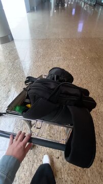 Individual pushing a luggage cart with a black bag through a spacious airport terminal with polished floors and modern architecture visible in the background