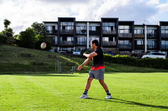 Player practices throwing a ball on a green field near a residential area in daylight