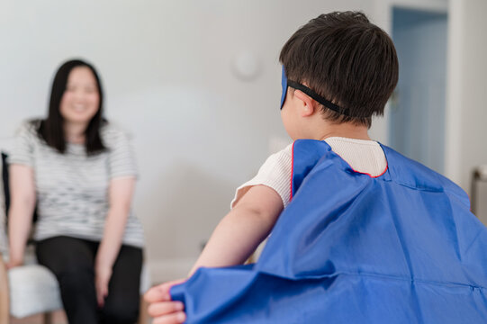 Asian boy in superhero costume doing pretend fly towards mum