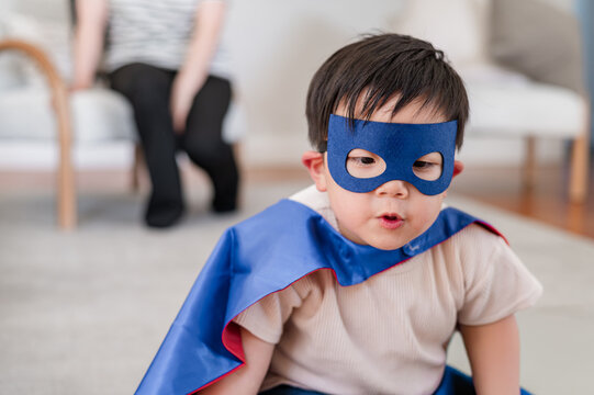Asian boy wearing superhero costume sitting on carpeted floor in the living room