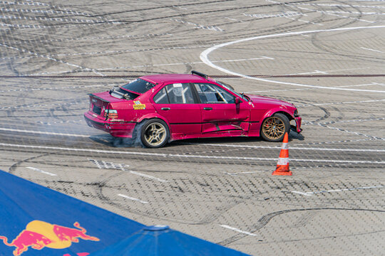 Vibrant red BMW car mid-drift on race track, outlined with orange cones and marked with white lines Bright natural light, casting dynamic shadows Signs of use on t - Kyiv, Ukraine 06-15-2025