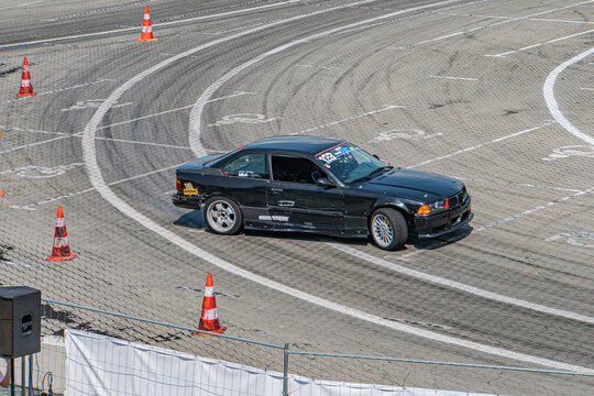 Black BMW car drifting on a race track with aerodynamic design, low-profile tires, white markings, orange traffic cones, chain-link fence, daytime, clear skies, dyna - Kyiv, Ukraine 06-15-2025