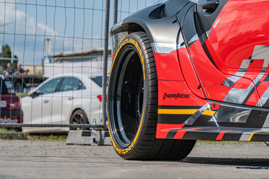 Close-up shot of a vibrant red Toyota Supra race car with bold black and white stripes, large wheels with silver rims, in a busy parking lot or environment The pers - Kyiv, Ukraine 06-15-2025