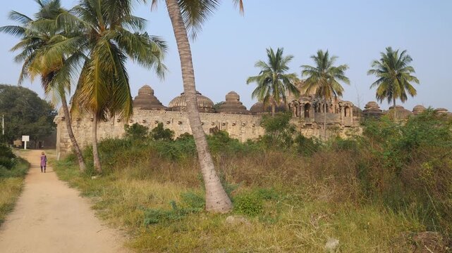 Panoramic view of Elephant Stables in Hampi, historic Vijayanagara architecture with domed chambers surrounded by palm trees and greenery in Karnataka, India