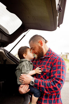 Father leaning forward touching foreheads with son seated on car boot
