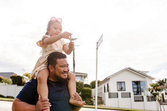 Samoan father carrying young daughter on his shoulders holding a toy aeroplane