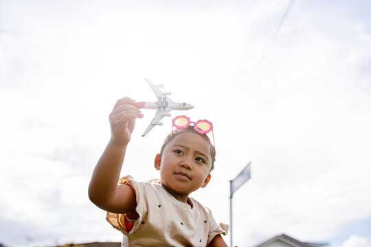 Young Samoan girl holding a toy aeroplane up in the air outdoors - travel concept
