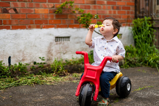Toddler boy on a tricycle blows bubbles in the backyard in New Zealand