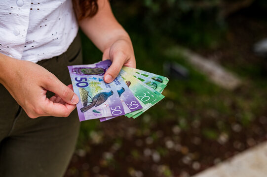 Adult woman holding New Zealand banknotes while standing outdoors in a garden