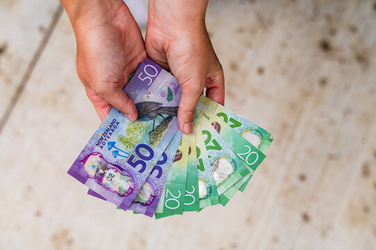 Adult hands display New Zealand banknotes under natural light