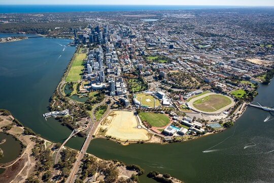 Aerial view of a city CBD and riverfront with a racecourse, parklands and bridge below.