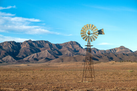 A rustic outback windmill stands before a dramatic mountain range on an arid plain