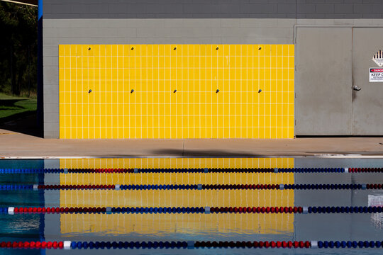 Yellow tiles of an outdoor shower at a public swimming pool with lane ropes in the foreground