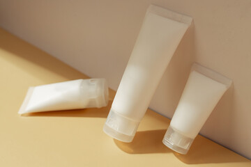 Minimal cosmetic tubes with skincare cream on pastel background in warm sunlight, beauty product packaging concept