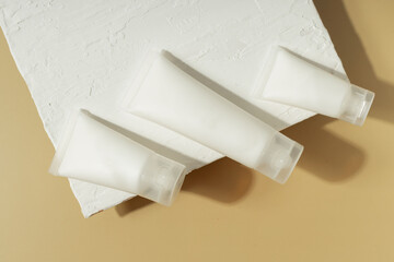 Minimal cosmetic skincare tubes on textured white surface with warm sunlight and shadows, beauty packaging concept