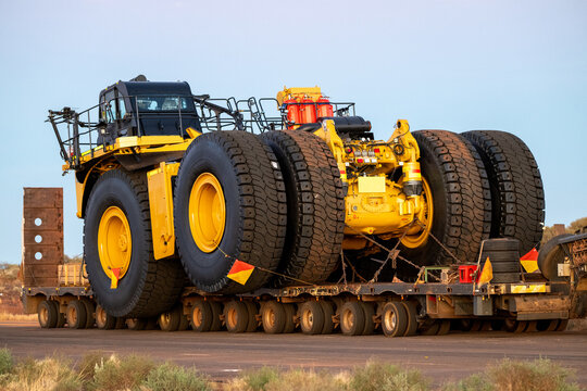 A massive yellow mining haul truck being transported on a heavy-duty low loader on an outback road