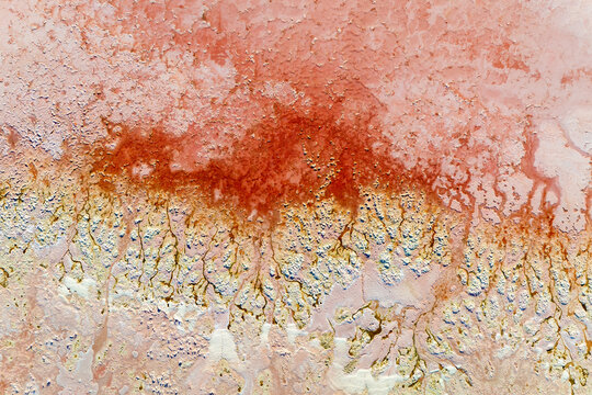 Close aerial shot of orange mineral veins branching across a pink and white salt surface