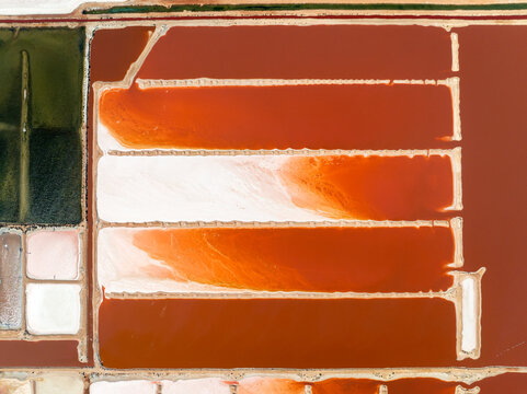 Top-down view of industrial salt evaporation ponds with vibrant red, orange, and white mineral hues