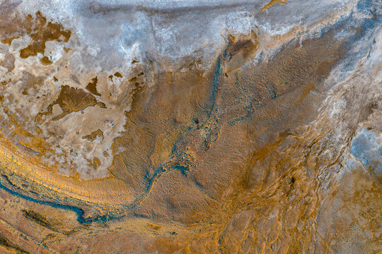 Aerial view of vibrant ochre sediment and deep blue erosion channels on a textured salt pan