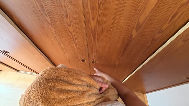 POV of a pregnant woman's hands and body closing a wooden wardrobe with children's clothes inside, holding children's coats in her arms.