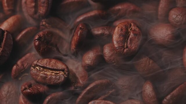 Macro process of roasting coffee beans with smoke on dark background, sliding shot top view.