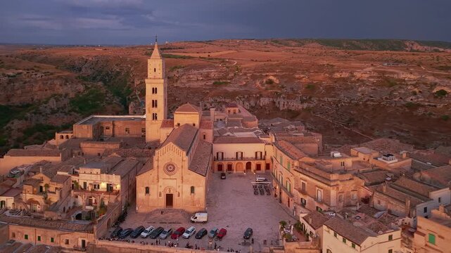 Aerial reveal of Matera at twilight as street lights turn on