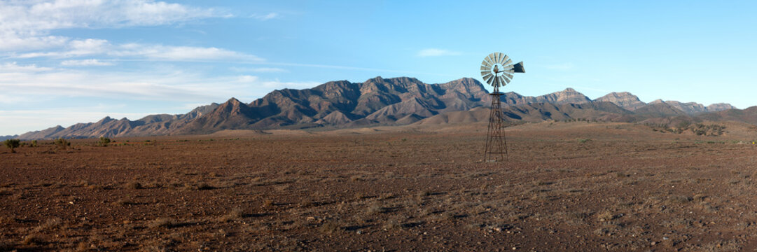 A vintage windmill stands on a stony plain against a rugged mountain backdrop
