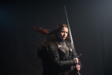 Ferce warrior woman with sword stands ready against dark backdrop © Fotokvadrat