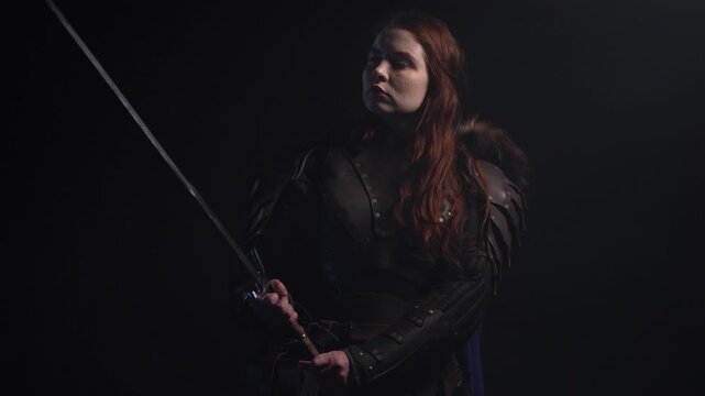 Fierce warrior woman with fiery hair and armor holds a sword against a dark background, exuding strength and determination