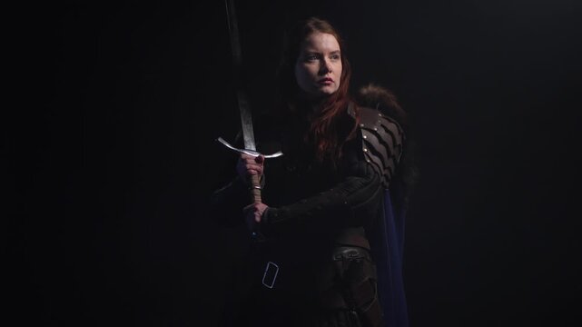 Fierce warrior woman with fiery hair and armor holds a sword against a dark background, exuding strength and determination