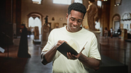 Man reading and flipping pages of a hardcover book with hands visible in a museum building, smiling...